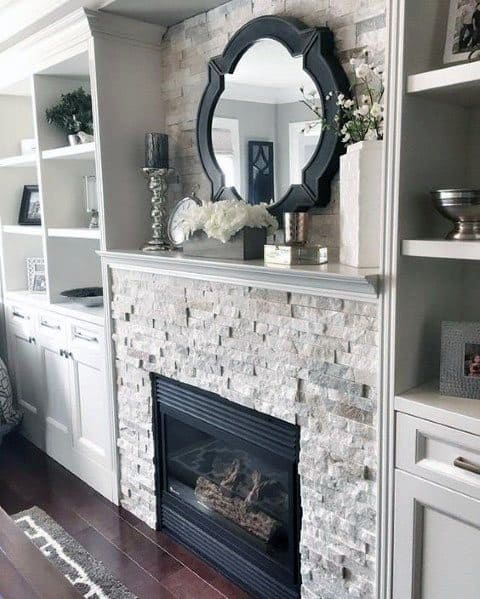 Chic stacked stone fireplace with built-in shelves, a black-framed mirror, and elegant decor accents