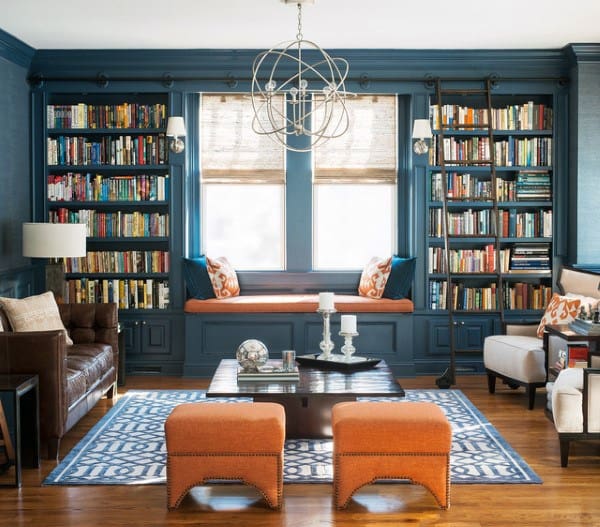 Cozy library with blue walls, bookshelves, a window seat, leather sofa, armchairs, and patterned rug