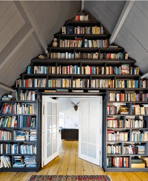 Bookshelves form a triangular shape above a doorway in a cozy room with wooden floors