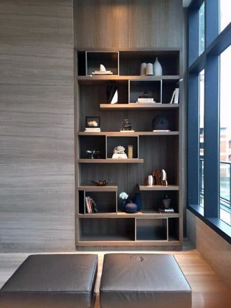 Wooden bookshelf with decorative items next to a large window, two leather cushions are on the floor