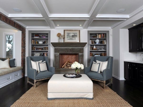 Cozy living room with two armchairs, a fireplace, bookshelves, and an ottoman on a woven rug