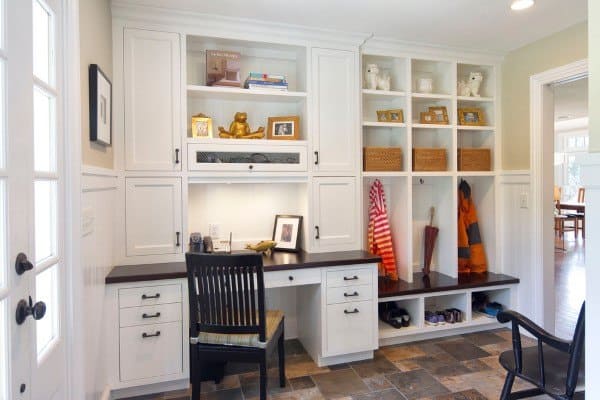 Home office with white cabinets, a built-in dark wood desk, shelves, chair; entryway bench with hooks and baskets
