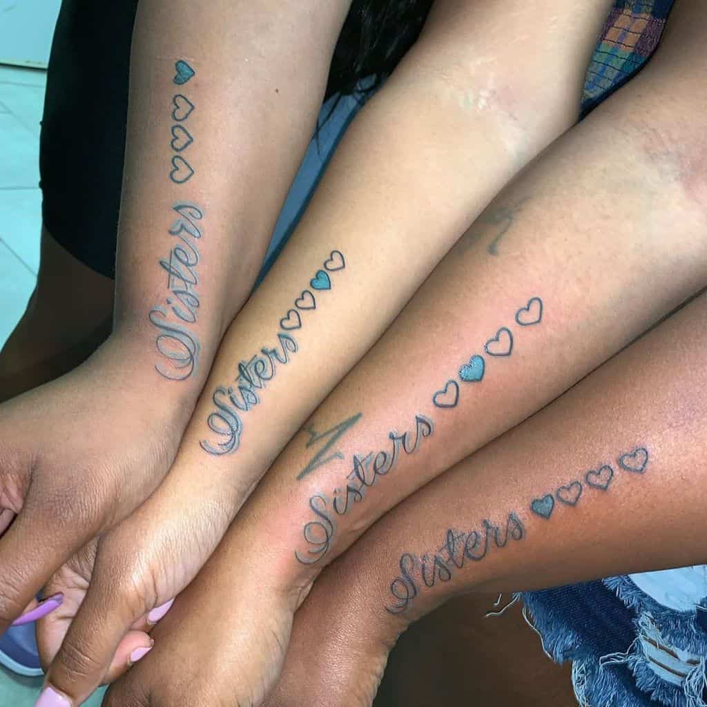 Matching sister tattoos featuring the word 'Sisters' in elegant script with four hearts, each uniquely shaded to represent individuality