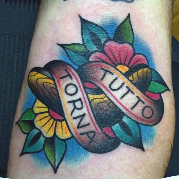 Traditional-style boomerang tattoo with flowers and a ribbon reading TUTTO TORNA, surrounded by bold colors and shading.