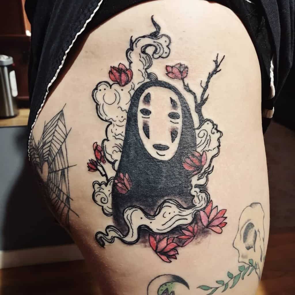 Bold Spirited Away tattoo of No-Face, surrounded by flowing smoke, red lotus flowers, and twisted branches for a mystical aesthetic