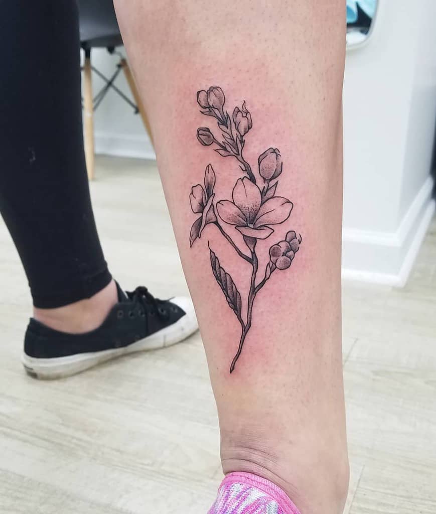Elegant black and grey tattoo of a lilac branch with fine-line shading and delicate blossoms, placed on the lower leg.