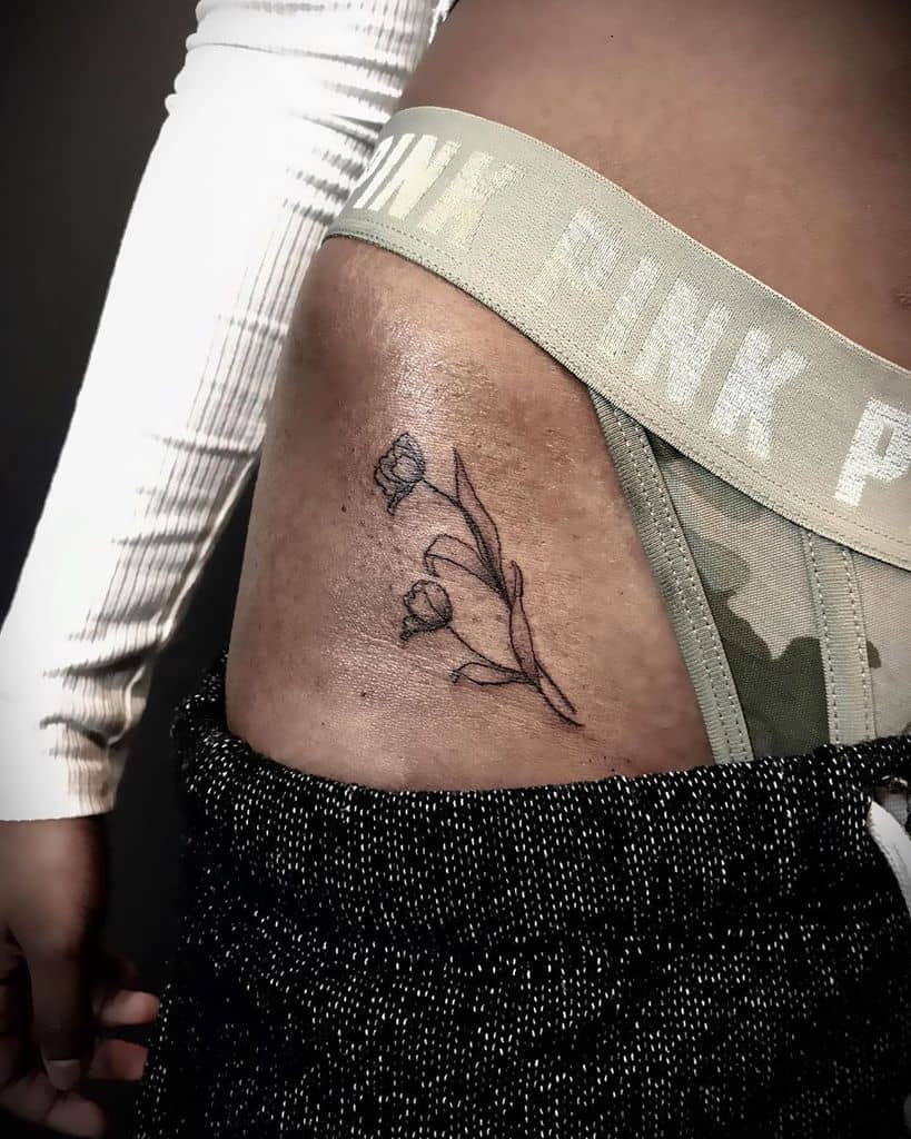 A delicate tulip tattoo on the side of the torso, featuring two blooming flowers with soft lines and gentle curves.