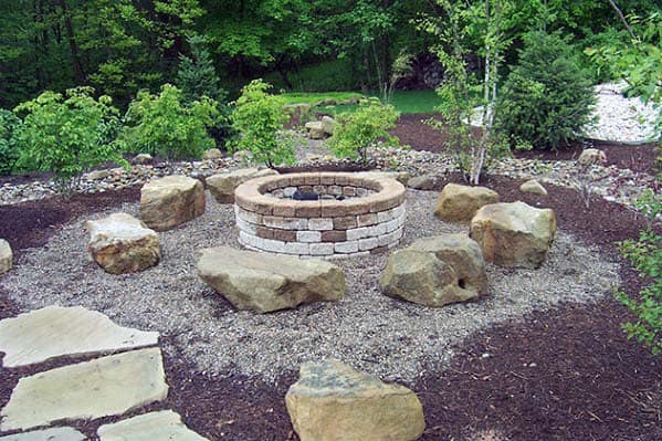 Stone fire pit surrounded by large rocks in a garden with trees and greenery