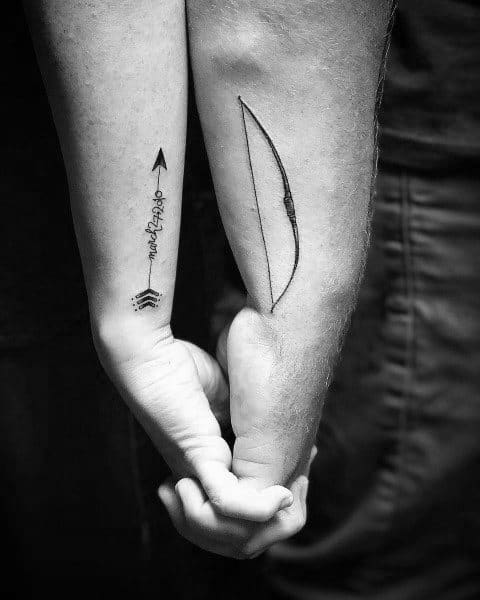 Matching couple tattoos of a bow and an arrow on forearms, symbolizing unity, direction, and love when brought together.