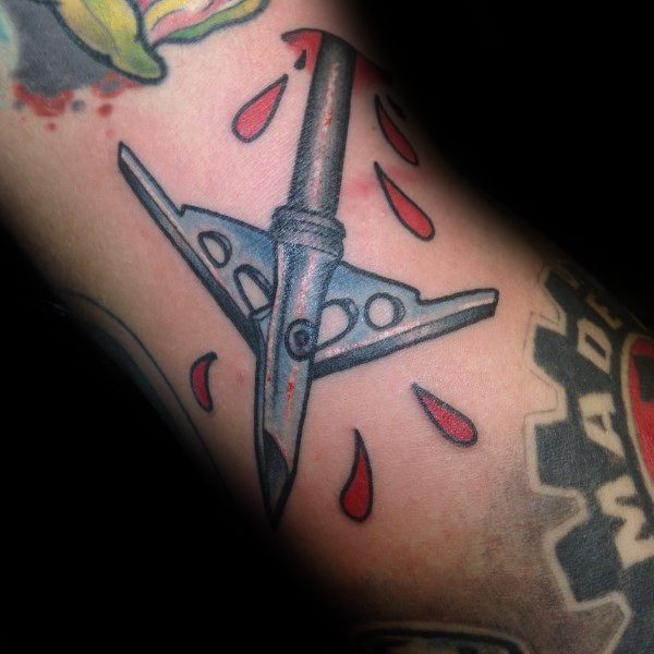 Colorful broadhead arrow tattoo with red blood drops, featuring bold outlines and a traditional style on the arm.