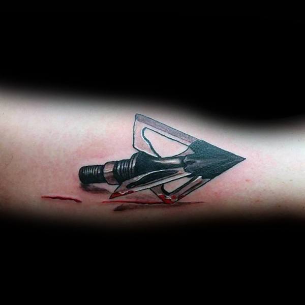 Realistic tattoo of a broadhead arrow tip on the skin with red ink to mimic blood, creating a 3D effect.