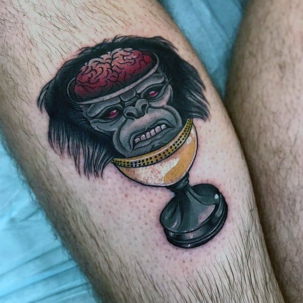 Indiana Jones-inspired tattoo featuring a monkey head with an exposed brain, resting on a golden chalice in bold, colorful design.