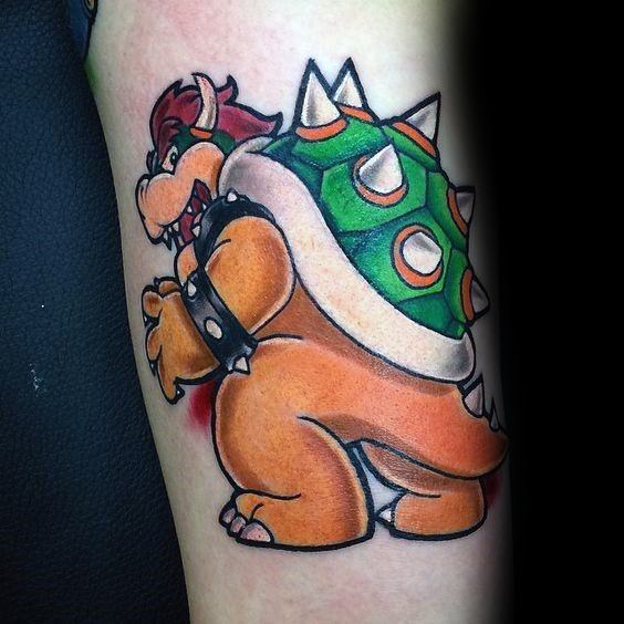 Classic Bowser tattoo on a man's arm with bold outlines, vibrant colors, and a playful pose capturing his iconic design from the Mario series.