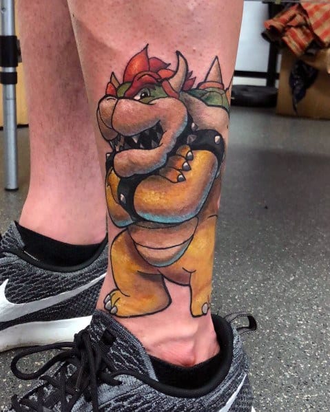 Bold Bowser tattoo on a man's ankle with vibrant colors, strong outlines, and a confident pose, creating a striking Nintendo-inspired design.