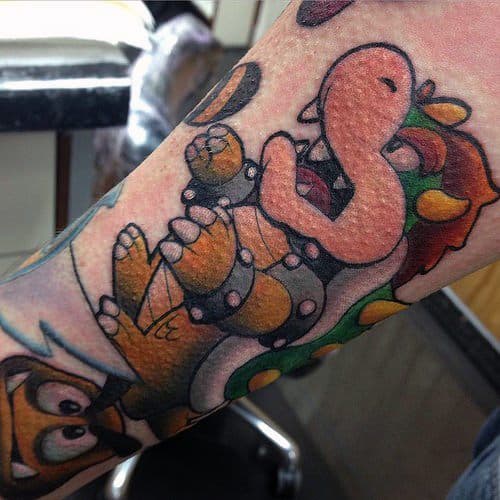 Cartoon-style Bowser tattoo on a man's arm with bold outlines, playful shading, and a dynamic pose, featuring a classic Mario-inspired look.