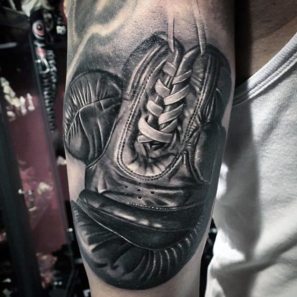 Hyper-realistic black and grey tattoo of a pair of hanging boxing gloves, detailed with laces and shadowing to create a 3D effect.
