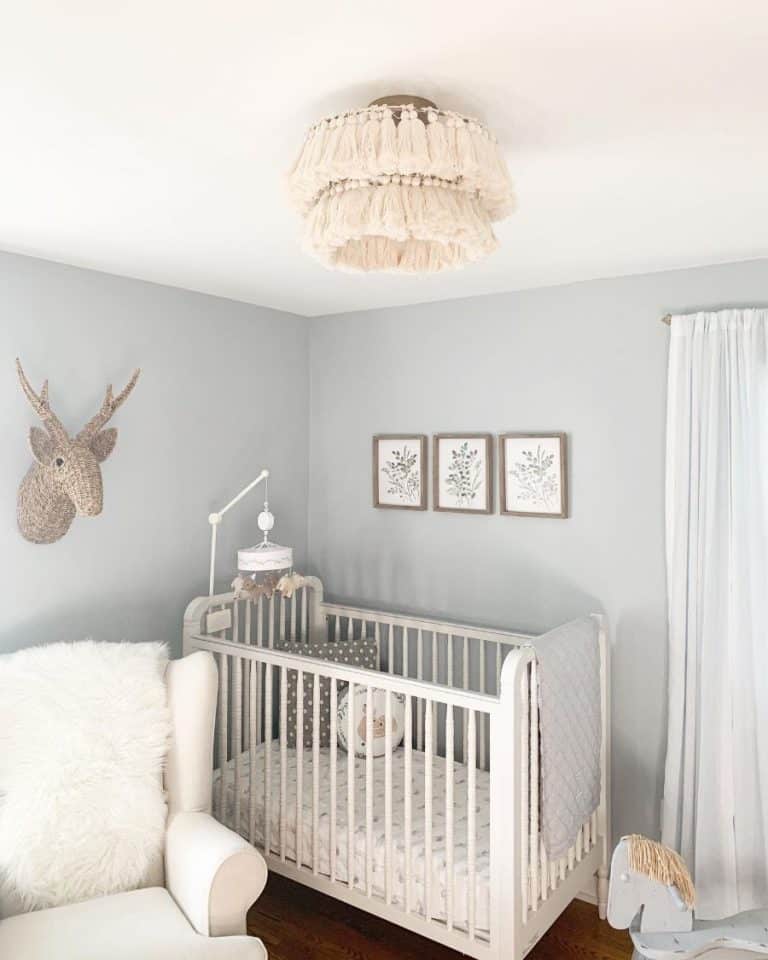 Nursery with white crib, moose head wall art, and tassel chandelier.