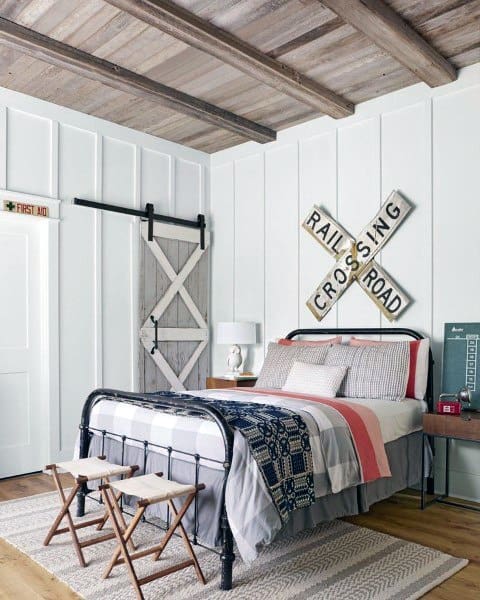 Cozy bedroom with a rustic metal bed, barn door, railroad crossing sign, and wooden beam ceiling
