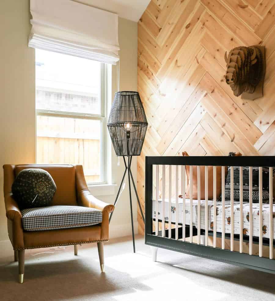 Rustic baby room with wood-paneled accent wall, modern black crib, and leather armchair.