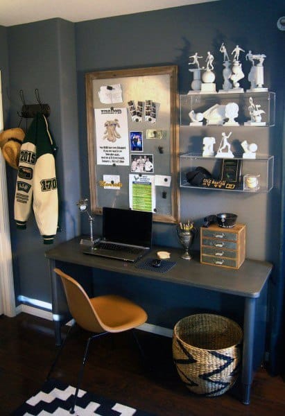 Cozy home office with laptop, bulletin board, sports memorabilia, and decorative shelves in a modern gray room