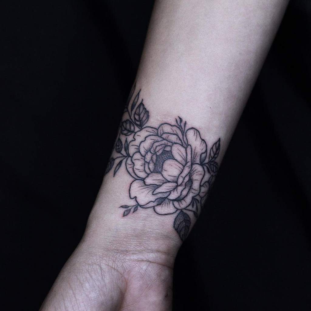 A black and white rose tattoo elegantly wraps around the wrist