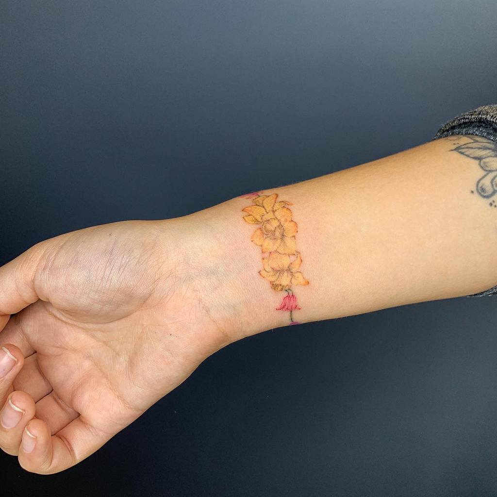 A beautifully crafted wrist tattoo featuring vibrant orange flowers gracefully cascading down, with a delicate pink bloom nestled at the base