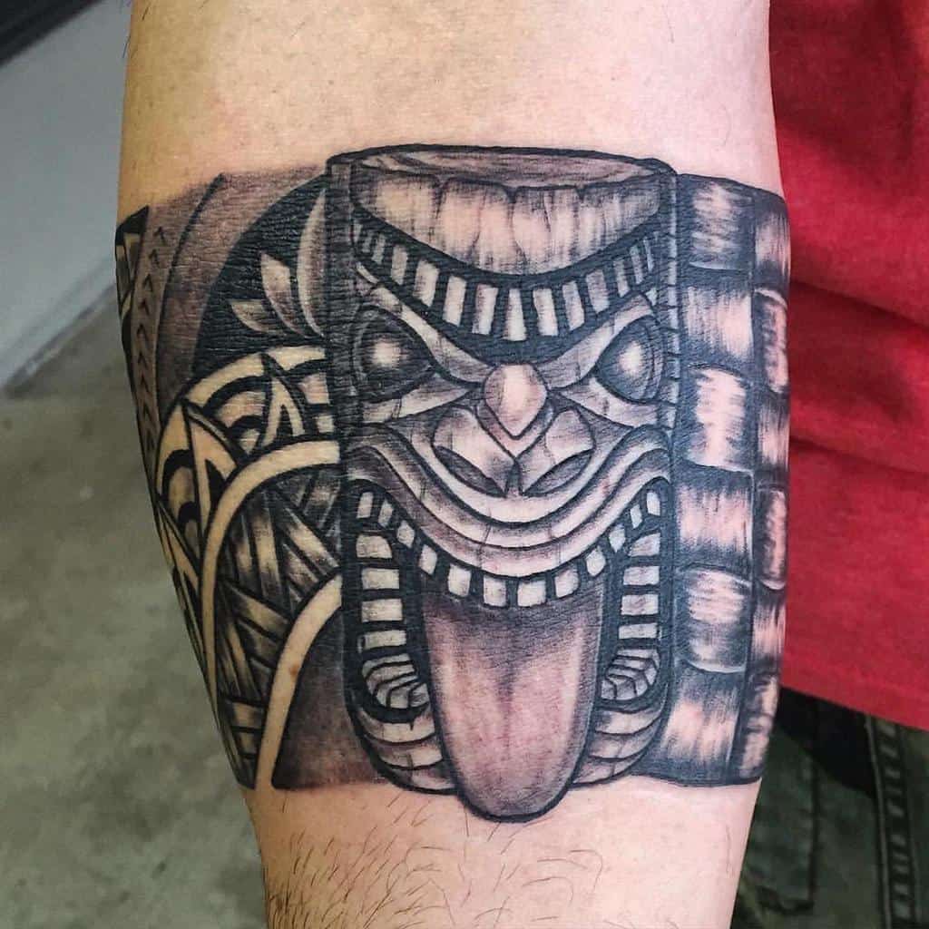 Black and grey Tiki tattoo, featuring a detailed mask with a protruding tongue