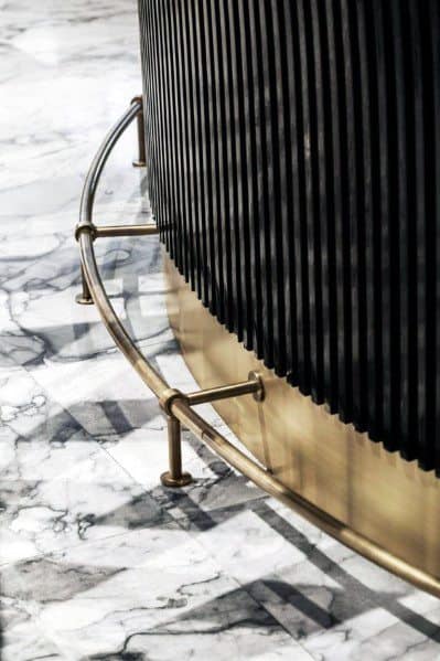 Curved brass foot rail around a black bar with a marble floor for a modern interior look.