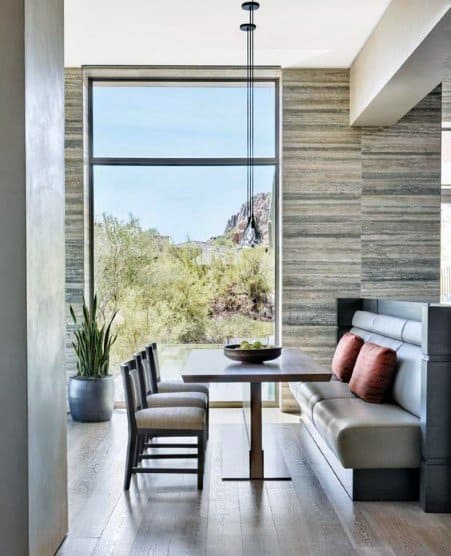 Modern nook with a cushioned bench, wooden table, and chairs, overlooking a large window with a desert view