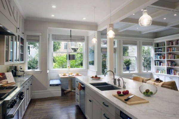 Bright kitchen with marble countertops, island, hanging lights, a cozy nook, and large windows overlooking a garden