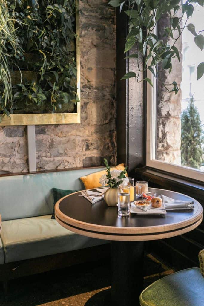 Cozy breakfast alcove with round table, light blue seating, and lush greenery wall.