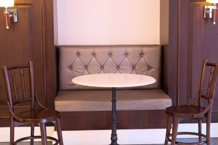 Elegant breakfast nook with tufted leather seating, round marble table, and wooden chairs.