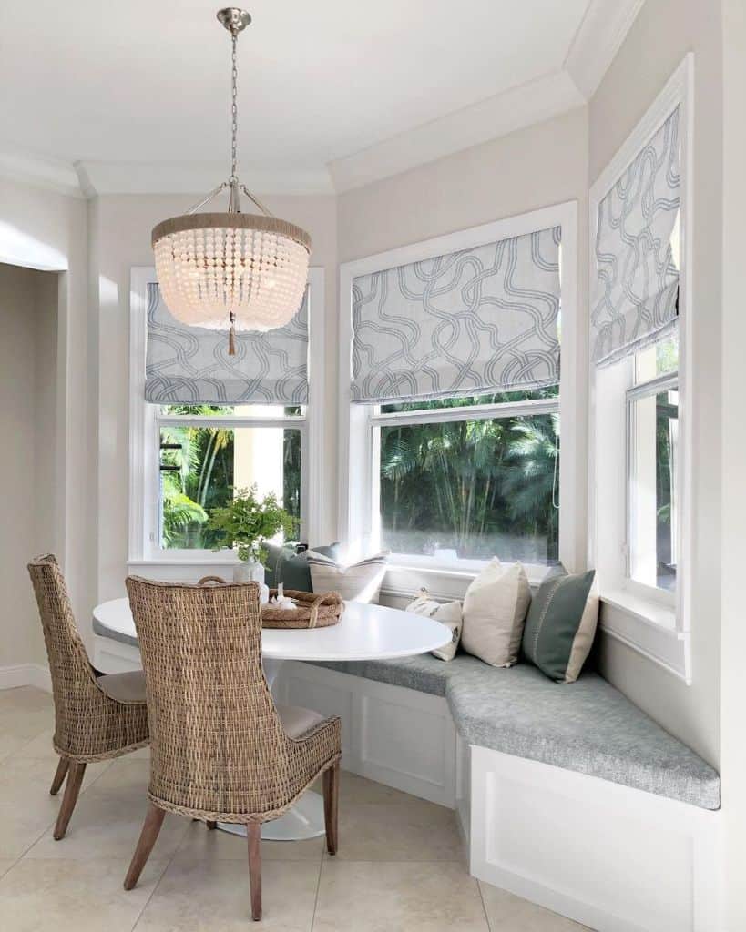 White and grey seating nook with round table, woven chairs, and a decorative chandelier.