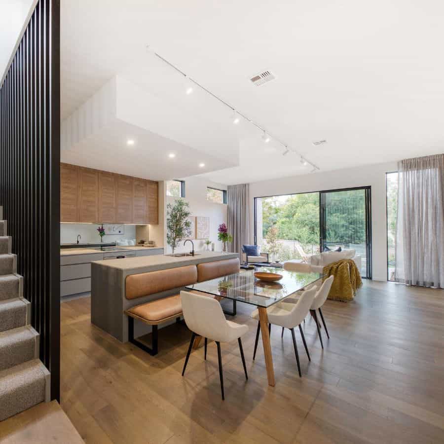 Large modern dining room with glass table, bench seating, and open plan kitchen layout.