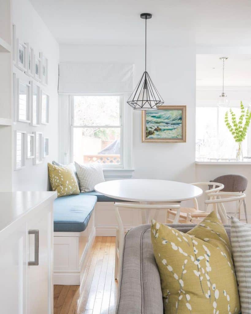 Bright breakfast nook with white table, chairs, and built-in seating with colorful pillows.