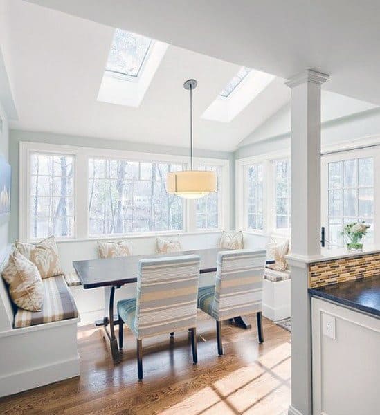 Cozy dining nook with skylights, white walls, a wooden table, cushioned bench seating, and striped chairs