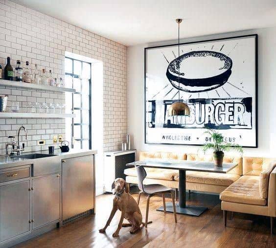 Modern kitchen with stainless steel, white tiles, a burger art piece, and a cozy dog nook by the wooden table and chairs