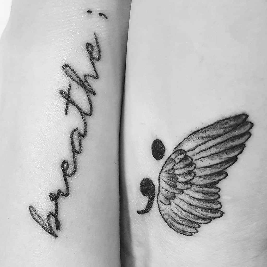 The tattoo features the word "breathe" with a semicolon at the end, and a second semicolon with wings, symbolizing freedom and resilience. The design evokes a sense of strength and encouragement.