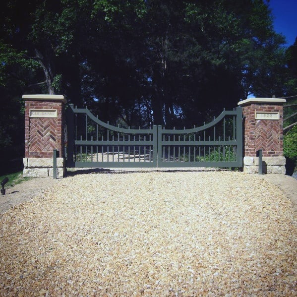 Green metal driveway gate with curved top design flanked by brick pillars.