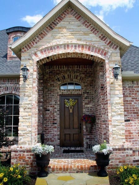 Charming entryway with mixed brick and stone cladding, an arched porch, wooden door, and decorative planters for a warm welcome