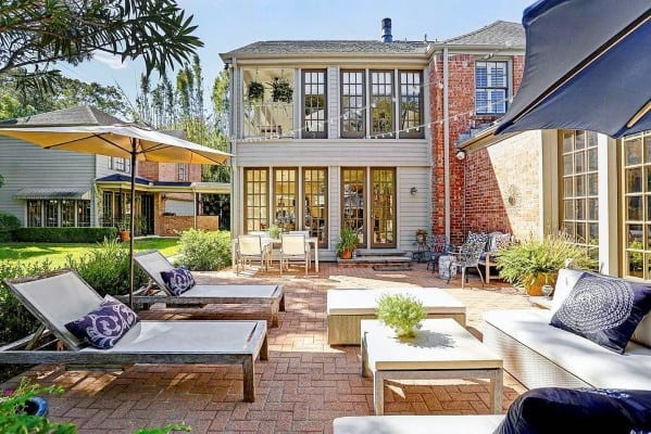 Sunny backyard patio with lounge chairs, umbrellas, and a charming brick house with large windows