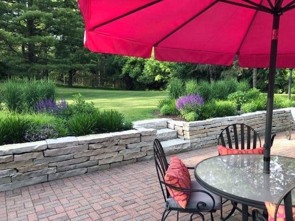 Patio with table, chairs, pink umbrella, and a garden view with brick wall and greenery