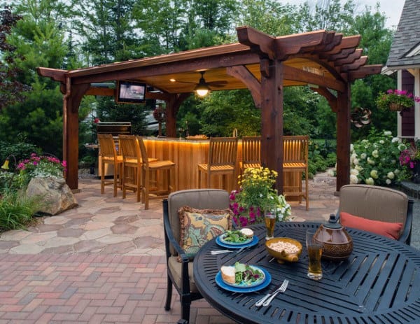 Wooden pergola with built-in bar, outdoor seating, and landscaped patio surrounded by greenery.