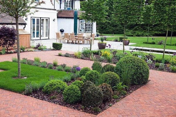 Modern garden with brick walkways, trimmed bushes, and outdoor dining near a white house