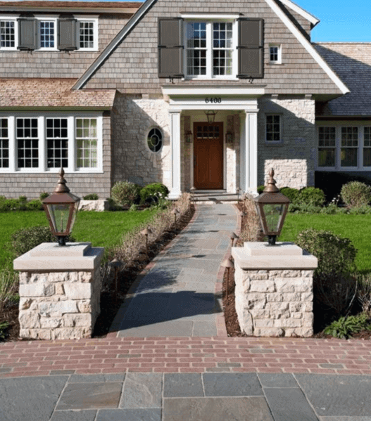 Charming front yard with a brick pathway, stone pillars, and traditional architecture leading to a welcoming front door
