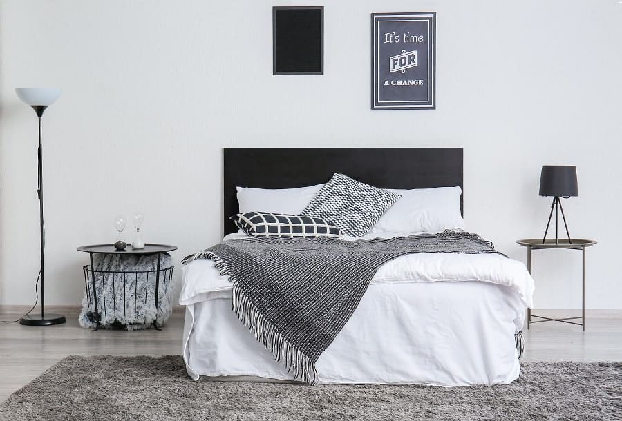 Minimalist bedroom with black headboard, monochrome bedding, and framed wall art.