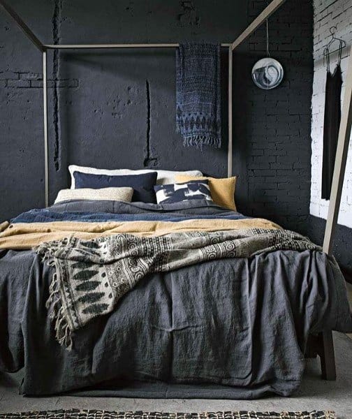 Rustic black bedroom with textured brick walls, layered bedding, and a minimalist canopy bed.