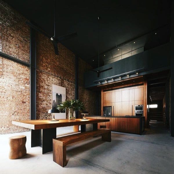 Industrial loft with exposed brick walls, wooden dining table, and modern black kitchen design.