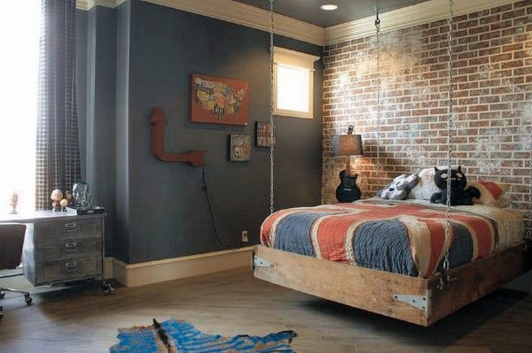 Industrial hanging bed with chains, rustic wooden frame, and brick accent wall in a teen bedroom.