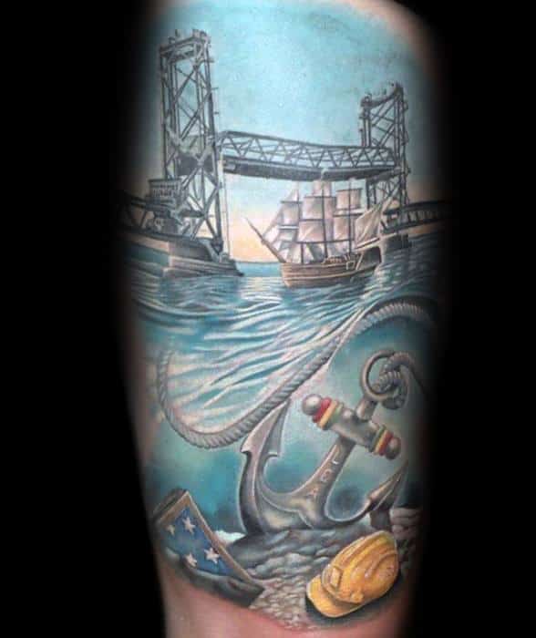 Tattoo of a maritime scene featuring a bridge, sailing ship, anchor, flag, and hard hat